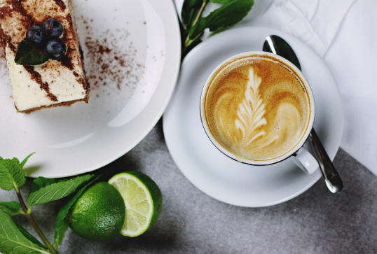 Café con leche y trozo de tarta sobre una mesa gris