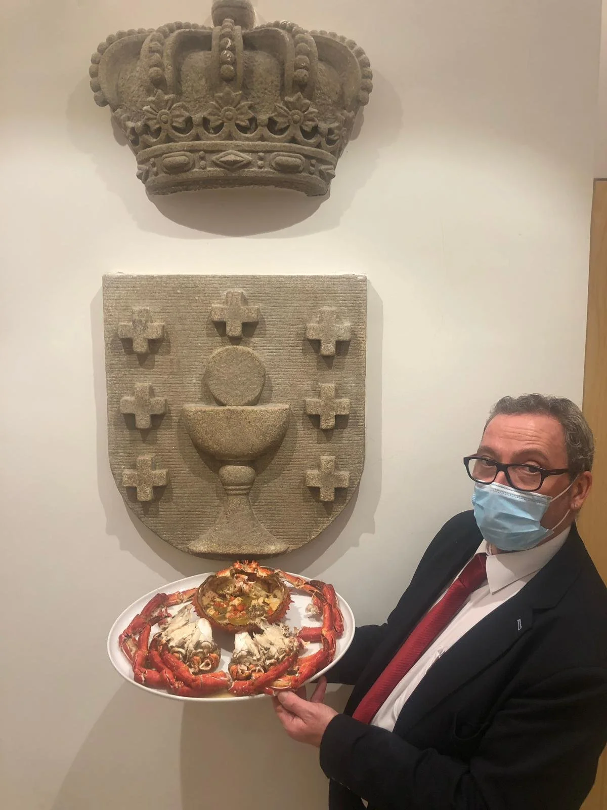 Camarero de Ogrelo con una bandeja de marisco junto a un escudo de piedra