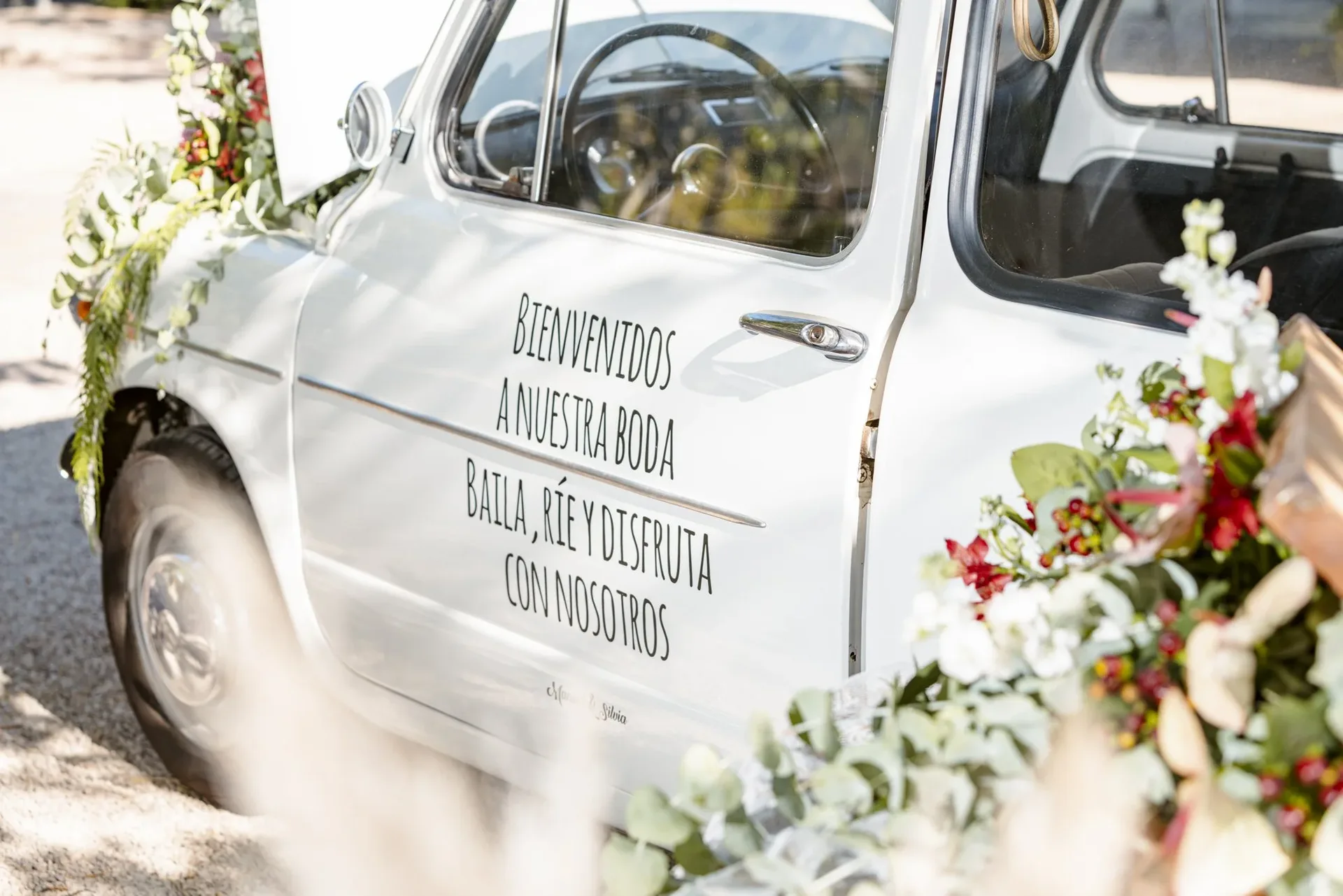 Coche clásico blanco decorado con flores y un mensaje de bienvenida a una boda