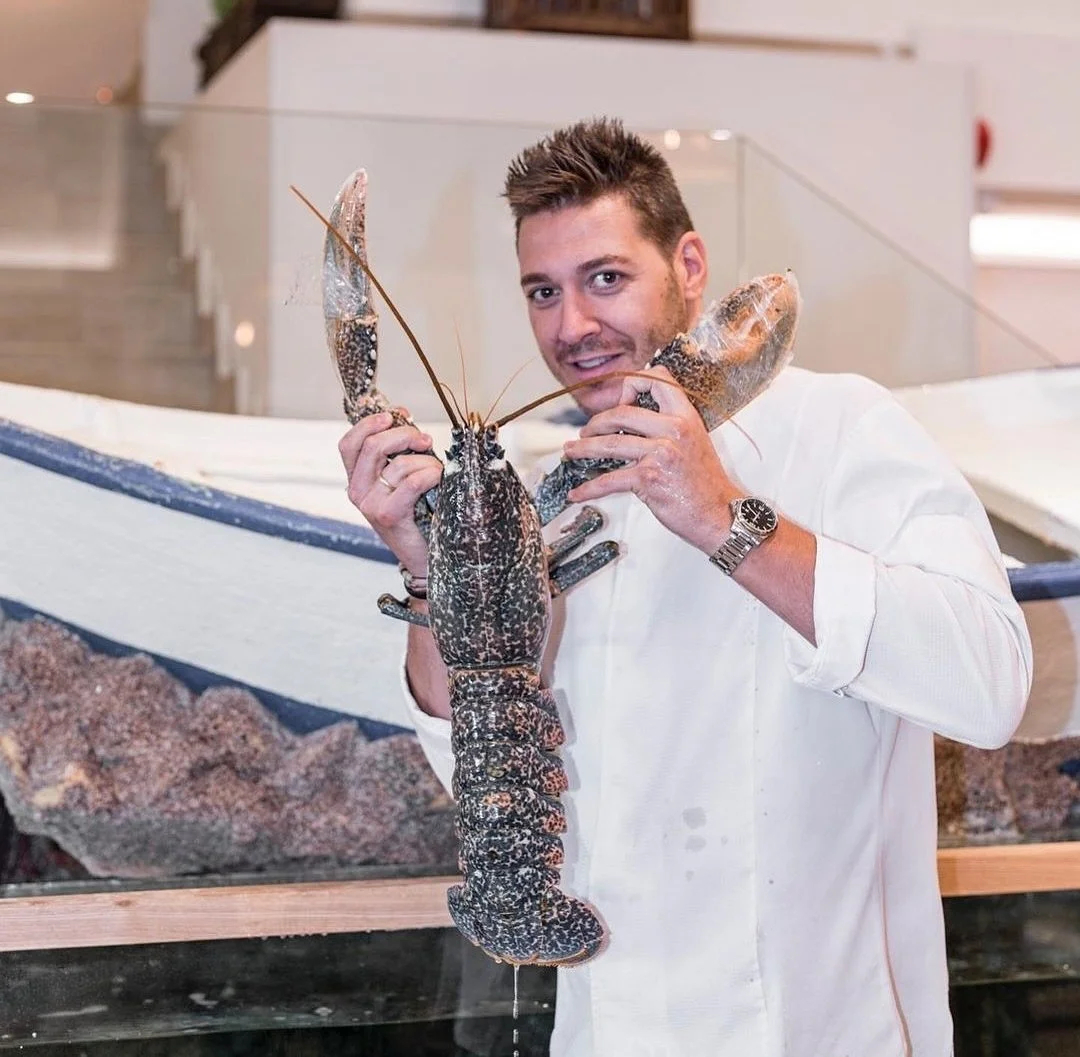 Cocinero de Ogrelo con un bogavante azul junto a una barca