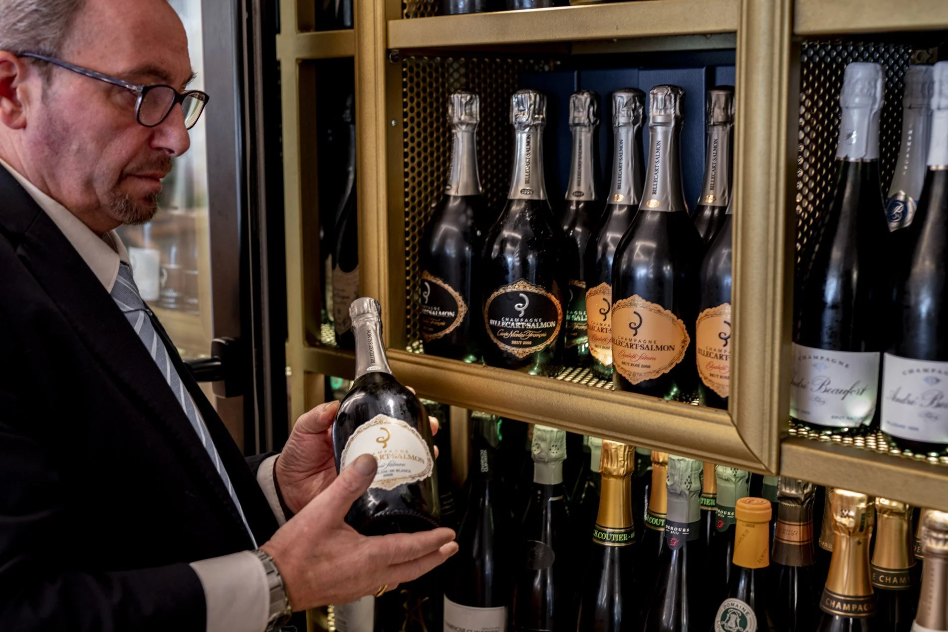 Sommelier de Ogrelo con una botella de champán junto a la vinoteca